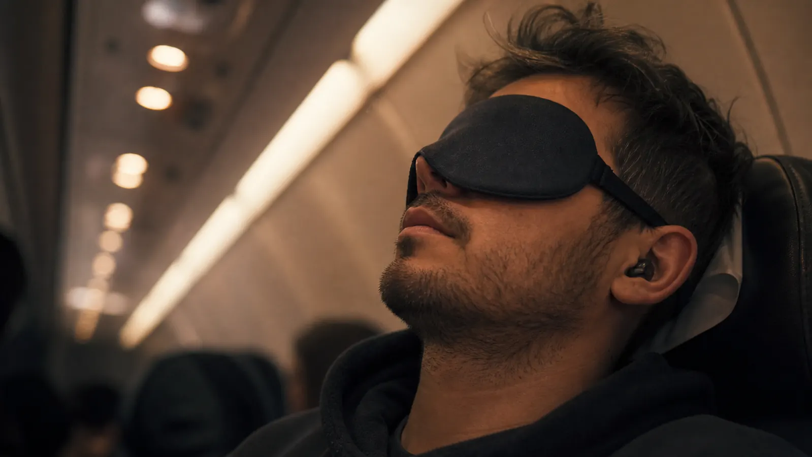 Traveler on an airplane resting with a sleep eye mask, cabin lights dimmed