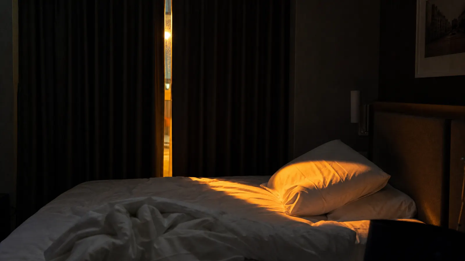 Streak of street lamp light entering a hotel room through a gap in heavy curtains at night