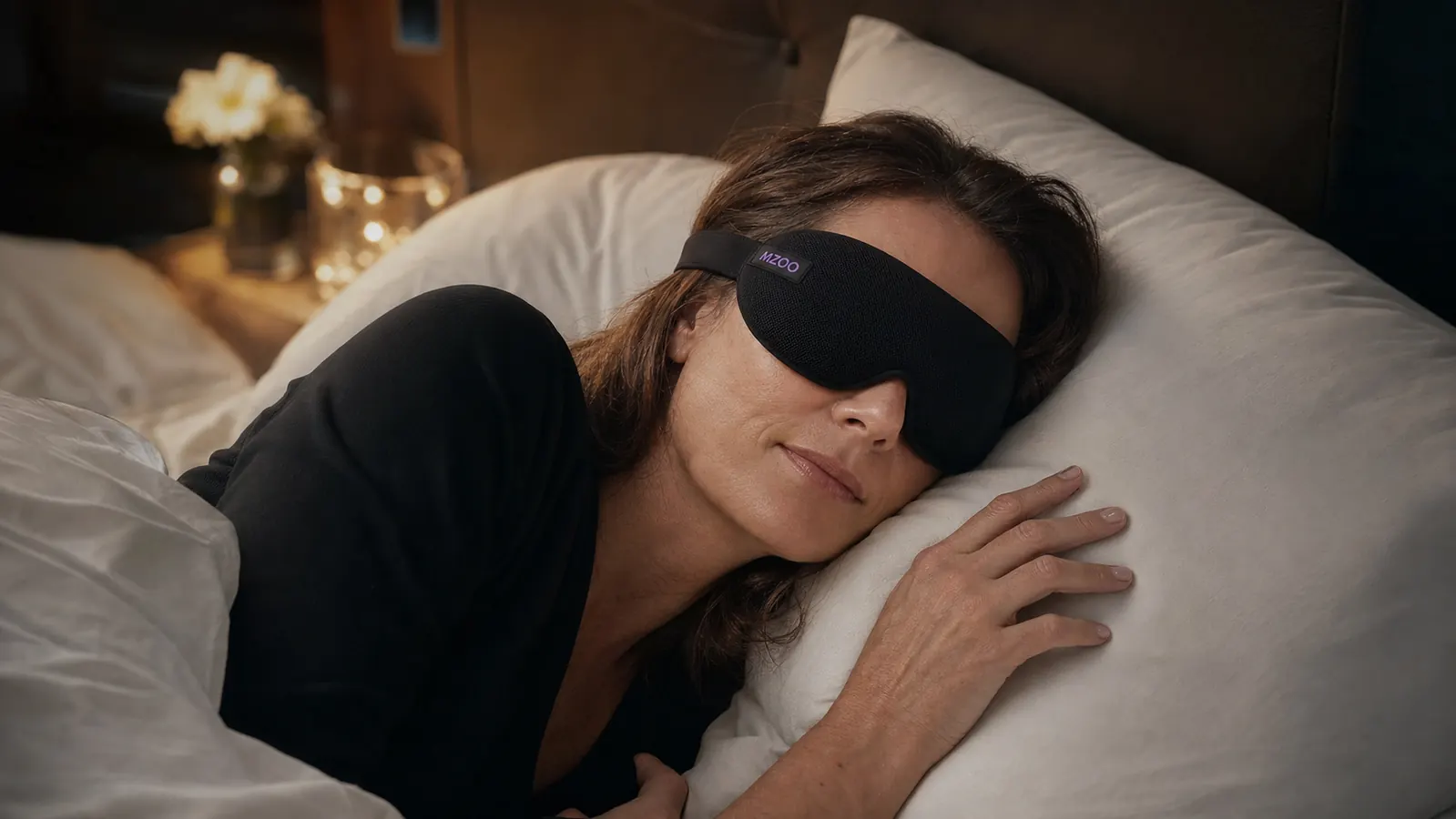 Person wearing a black 3D contoured sleep eye mask while lying in bed, appearing deeply relaxed